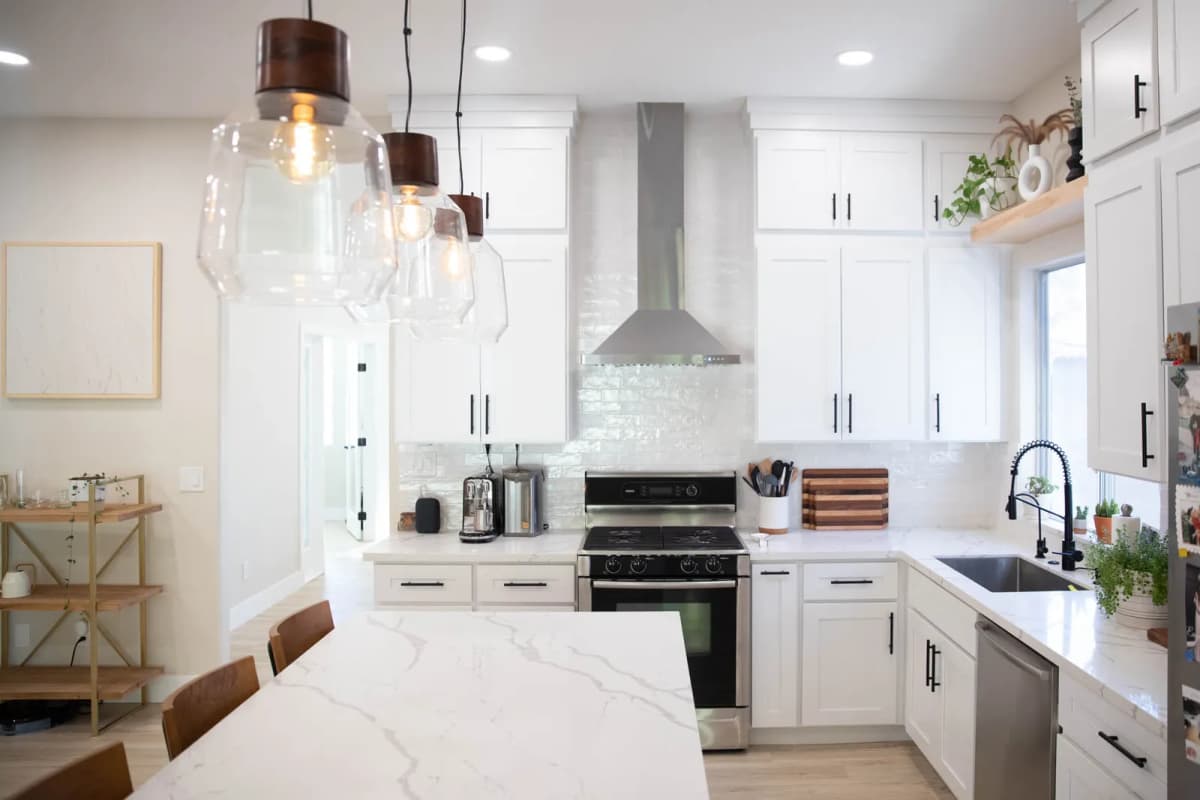 Range wall with stainless chimney hood and stacked white shaker cabinets