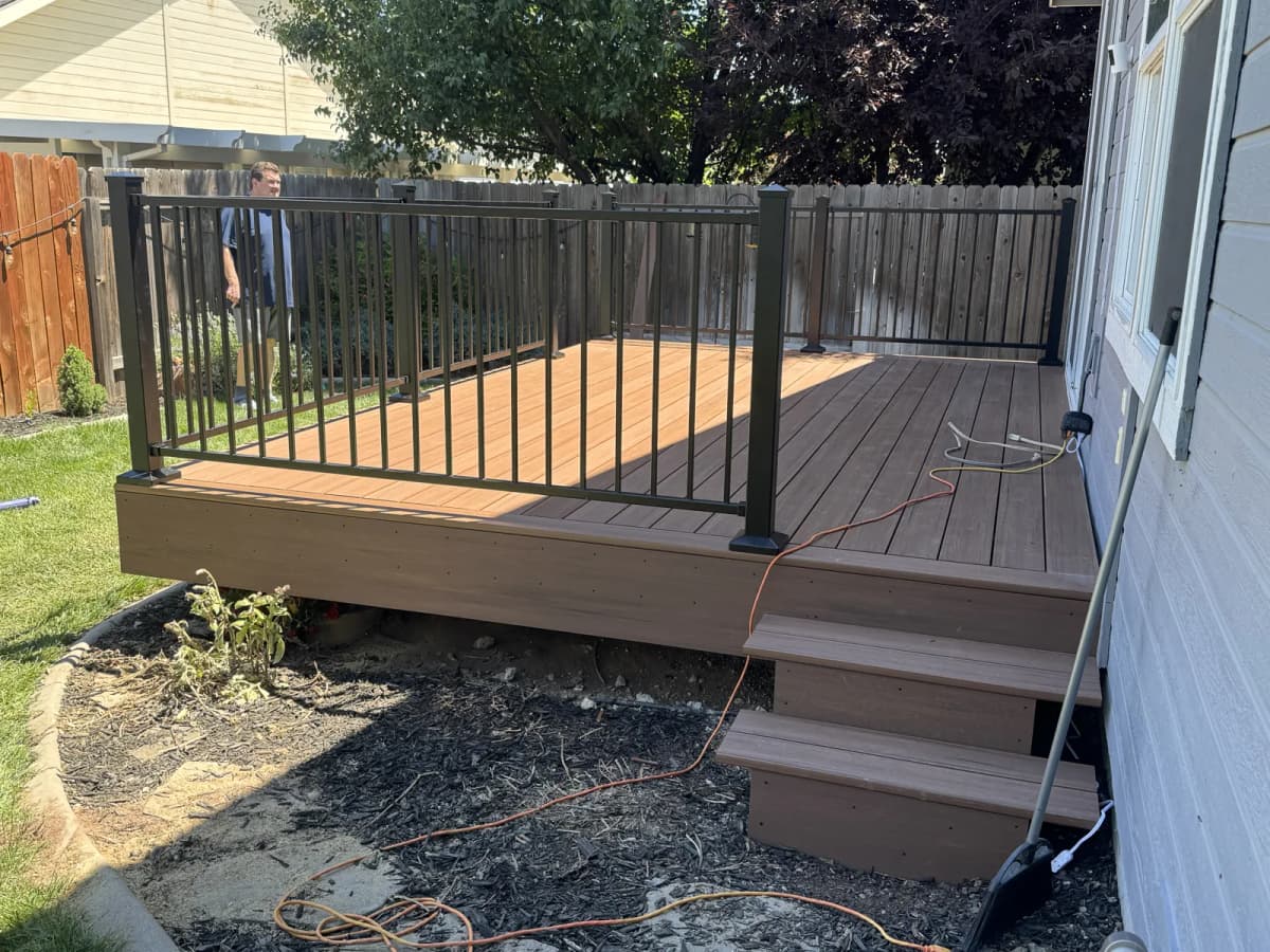 Side view of a new TimberTech composite deck with metal railing against a gray Boise house